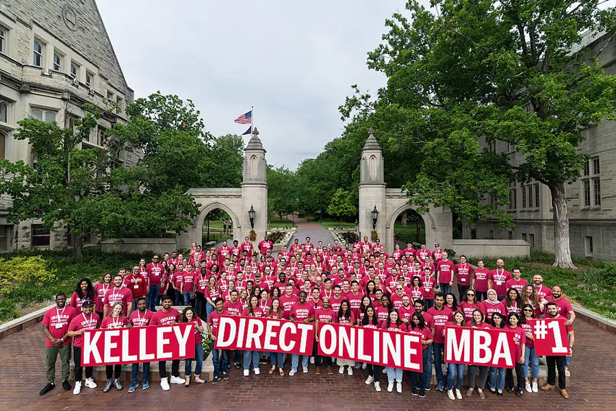A group of students stands in front of Sample Gates holding a sign that says Kelley Direct.