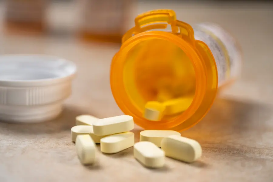A prescription bottle lays open on a table with pills spilling out of it.