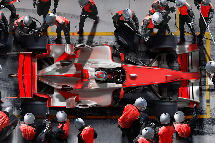 A race car is pictured from above, a pit crew wearing matching red uniforms surrounds the car.
