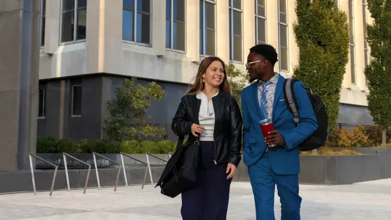 Two student interns walk across a business courtyard while talking.
