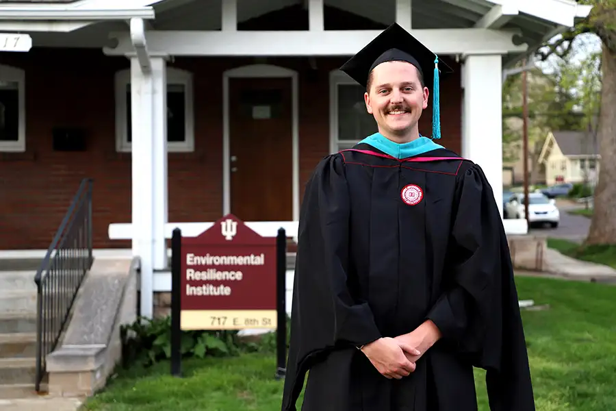 A person stands in a cap and gown in front of the Environmental Resilience Institute.