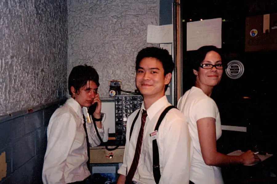 A nostalgic photo of three people, one person speaks on the phone while a man and woman look back at the camera smiling.