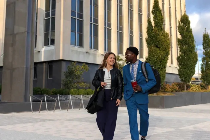 Two student interns walk through a business courtyard, a glass-walled building stands behind them.