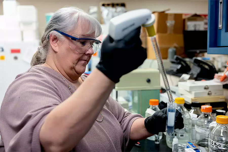 A researcher wearing goggles fills a test tube.