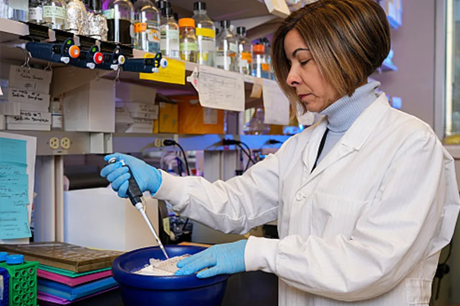 woman in a white lab coat puts liquid in a beaker