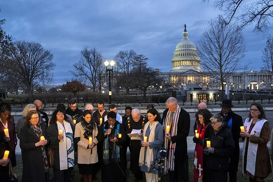 A group of people holding candles stand together, the United Stated Capitol building in the background