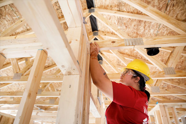 An IU community member wearing a hardhat and goggles contributes to the construction of a house.