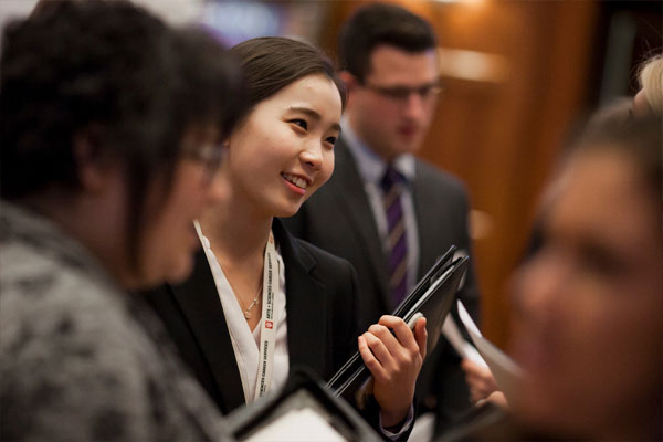 A professionally-dressed student holding a portfolio networks with colleagues.
