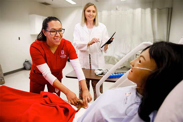 A nursing instructor provides direction to a student interacting with a medical manikin