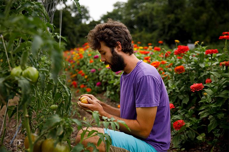 Student inspecting vegetables in a garden.