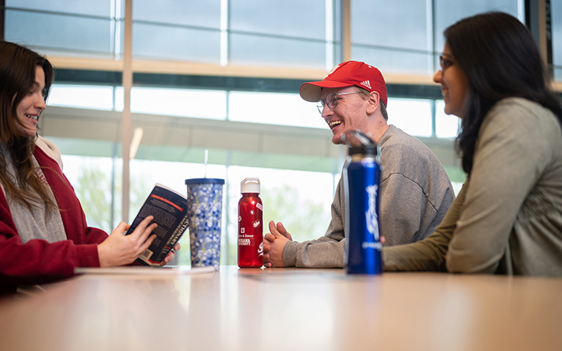 Three students talk and smile while sitting around a table.