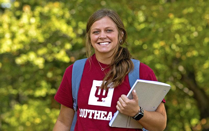 A smiling student in an IU Southeast T-shirt holds a notebook.