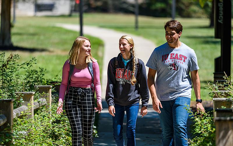 Three students walk near greenery on IU East’s campus. Two of them wear IU East shirts.