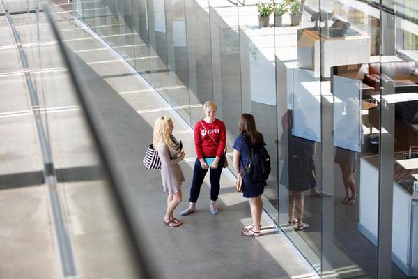 Three female students standing in a long curved hallway on IUPUC campus.