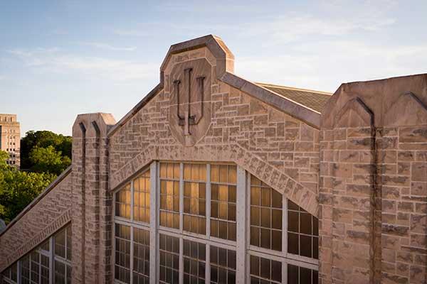 A limestone trident adorns the side of the Bill Garrett Fieldhouse during a summer day on the Indiana University Bloomington campus.