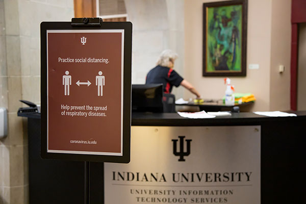 A maintenance worker disinfects a desk behind sign encouraging people to practice social distancing at the IMU.