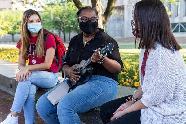 Three female undergraduate students sitting outside with masks on.