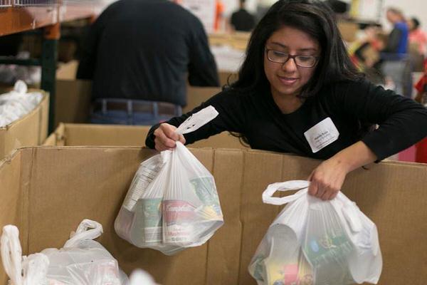 Student putting bags of groceries into a cardboard box.