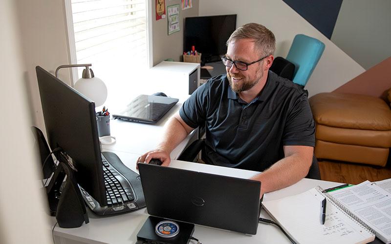 A male student sits at his home computer desk.