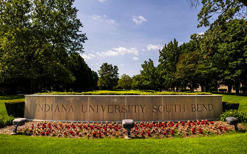 A limestone sign for Indiana University South Bend that is surrounded by landscaping and trees