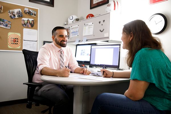 A counselor sits at his desk and smiles as he meets with a student in the counseling office.