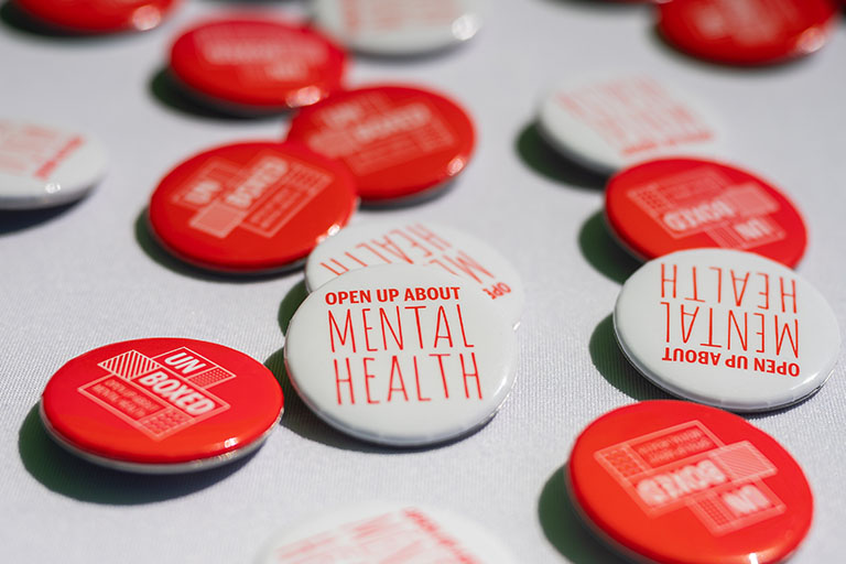 Pins lying on a surface which read "Open up about mental health"
