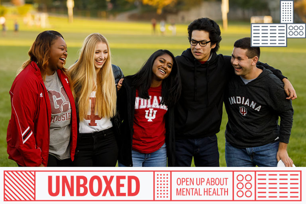 a group of students of various races and genders, stand together with their arms around each other. They are smiling and supporting each other.